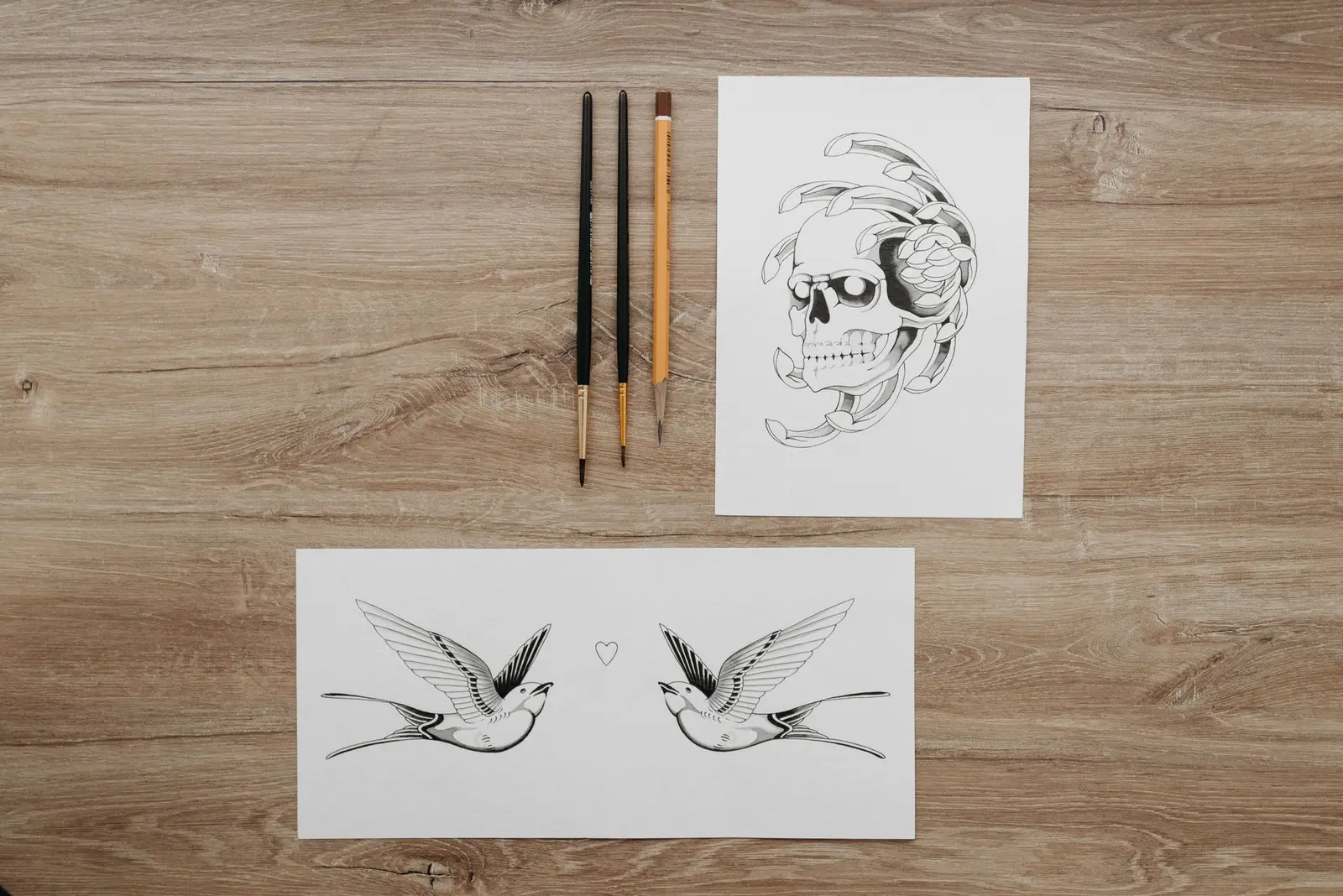 Skull and swallow tattoo flash next to brushes