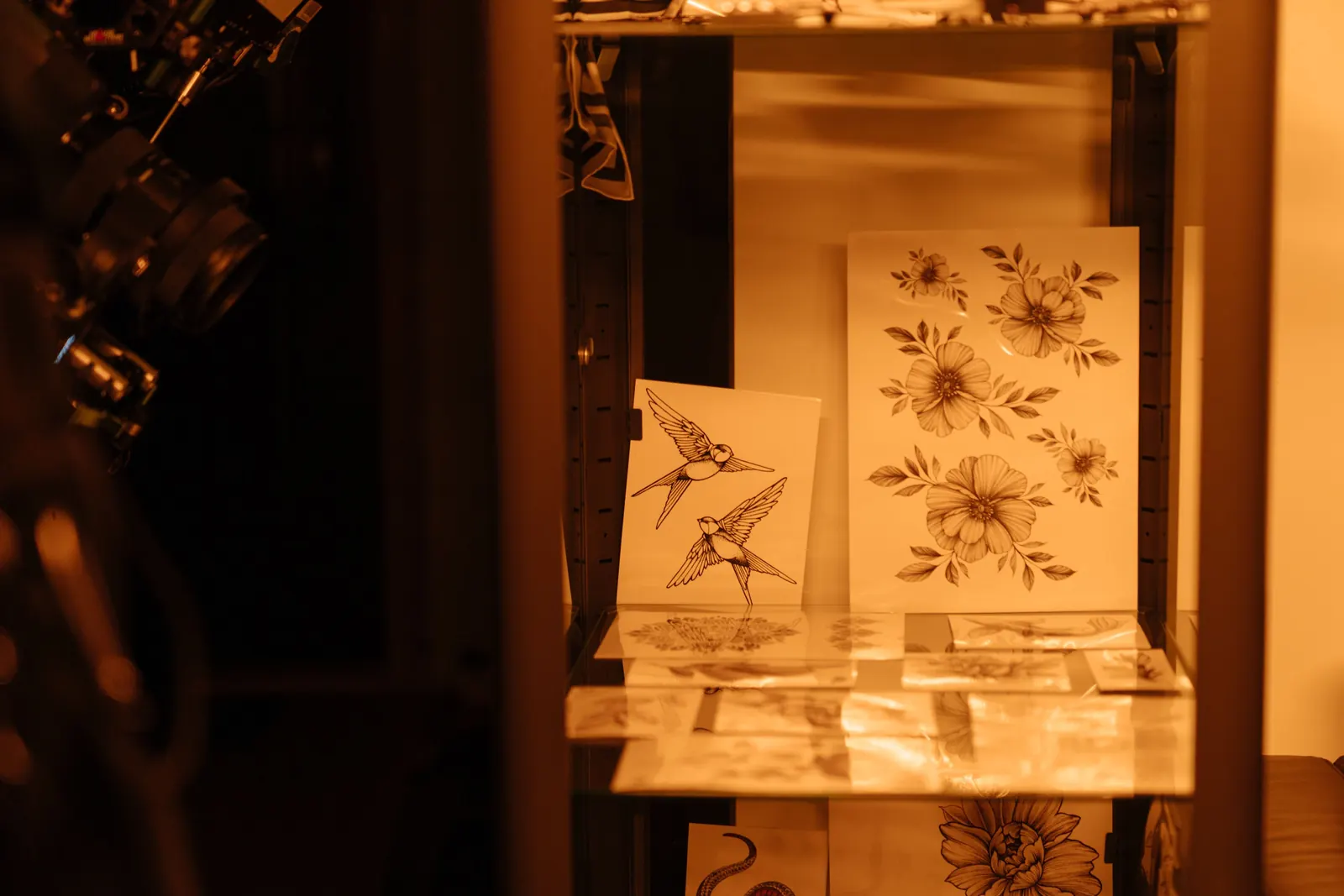 Floral and swallow flash designs displayed in a warmly lit tattoo shop