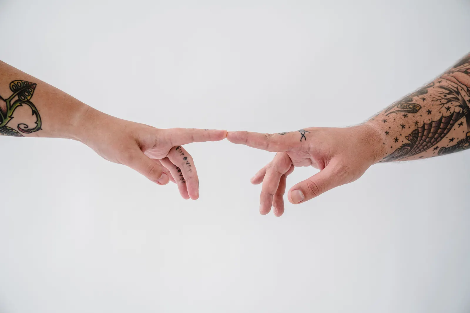 Two tattooed hands reaching for each other against a white background