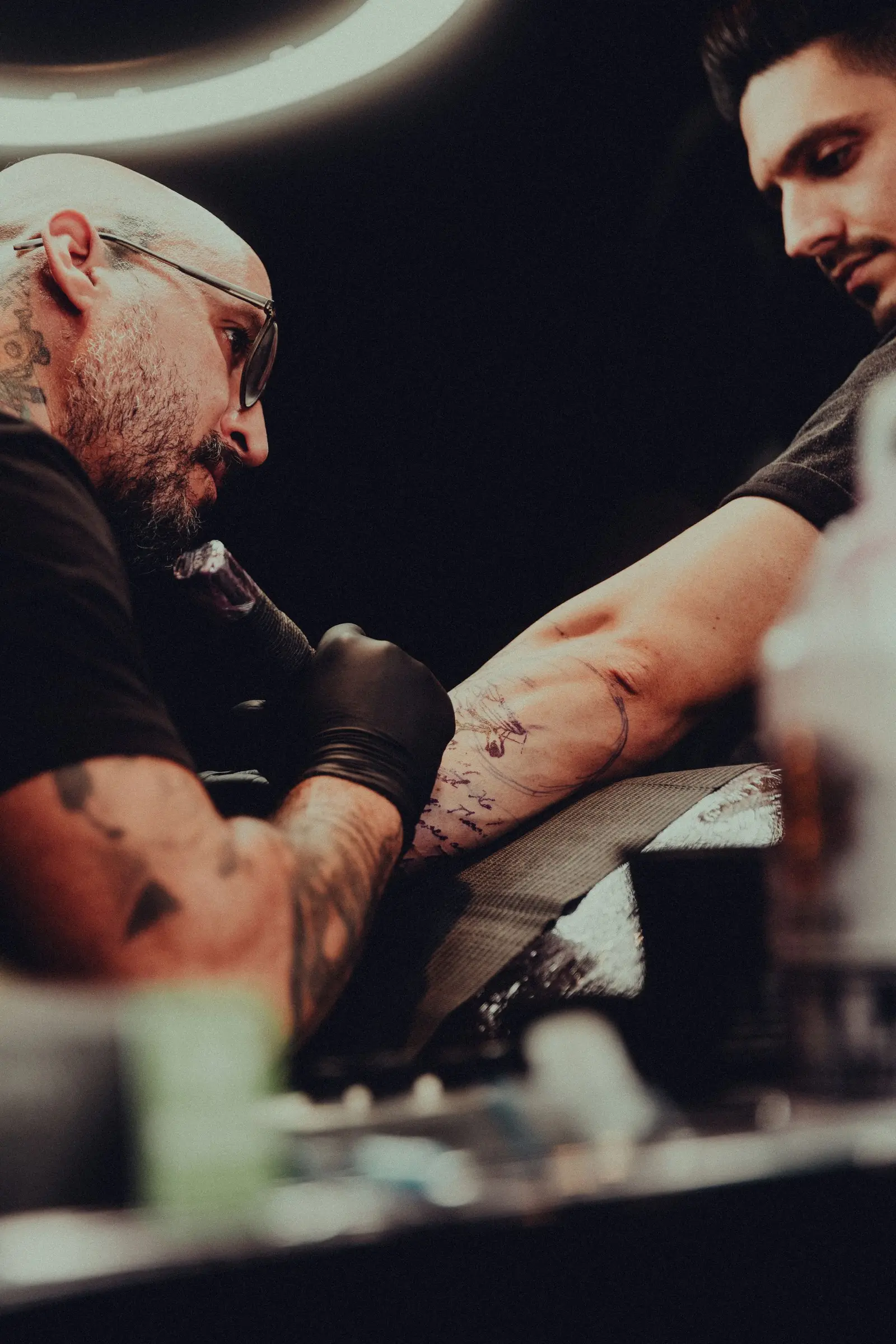Tattoo artist working on a detailed arm tattoo in a dark studio