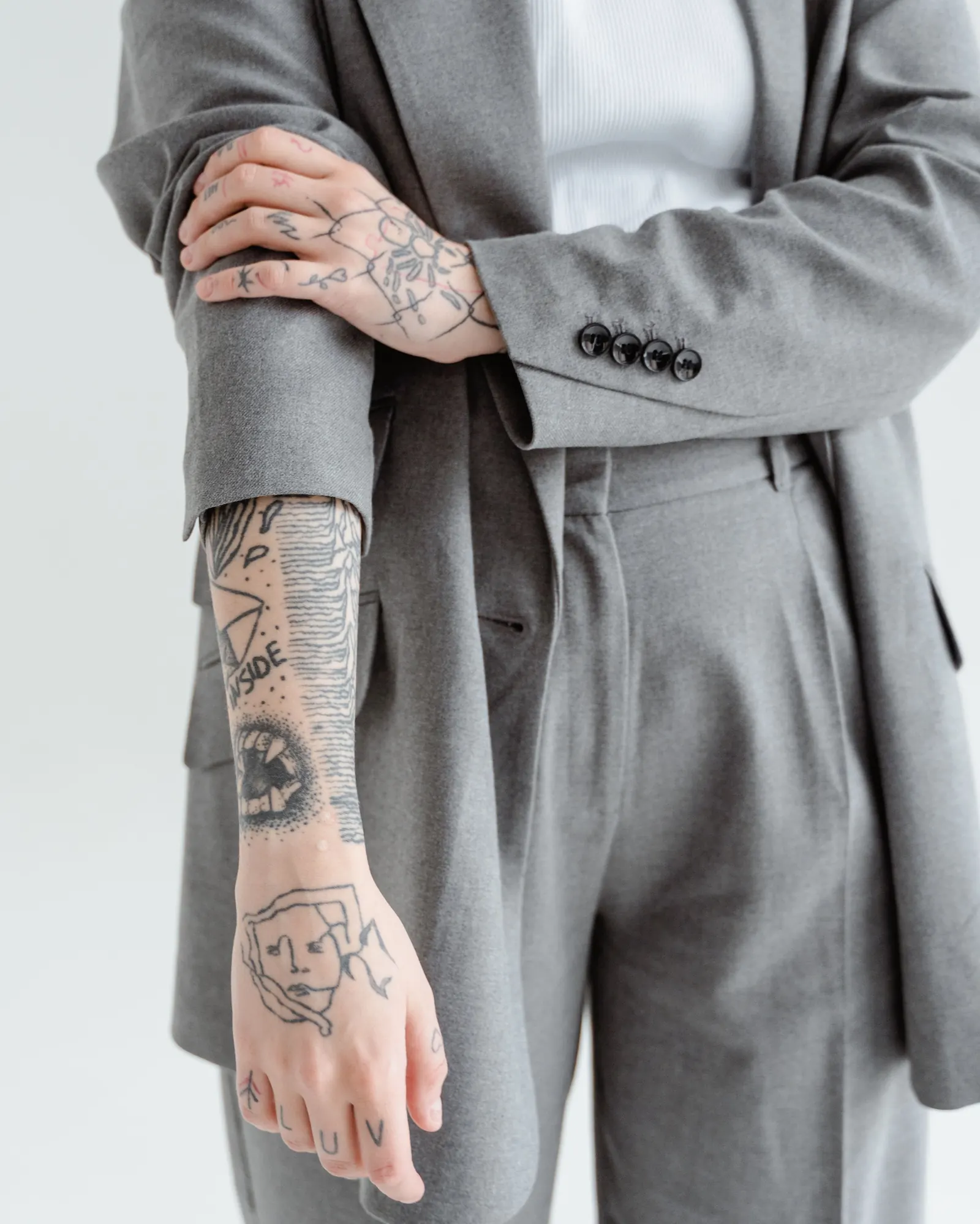 Person in a grey suit rolling up a sleeve to show fine-line tattoos
