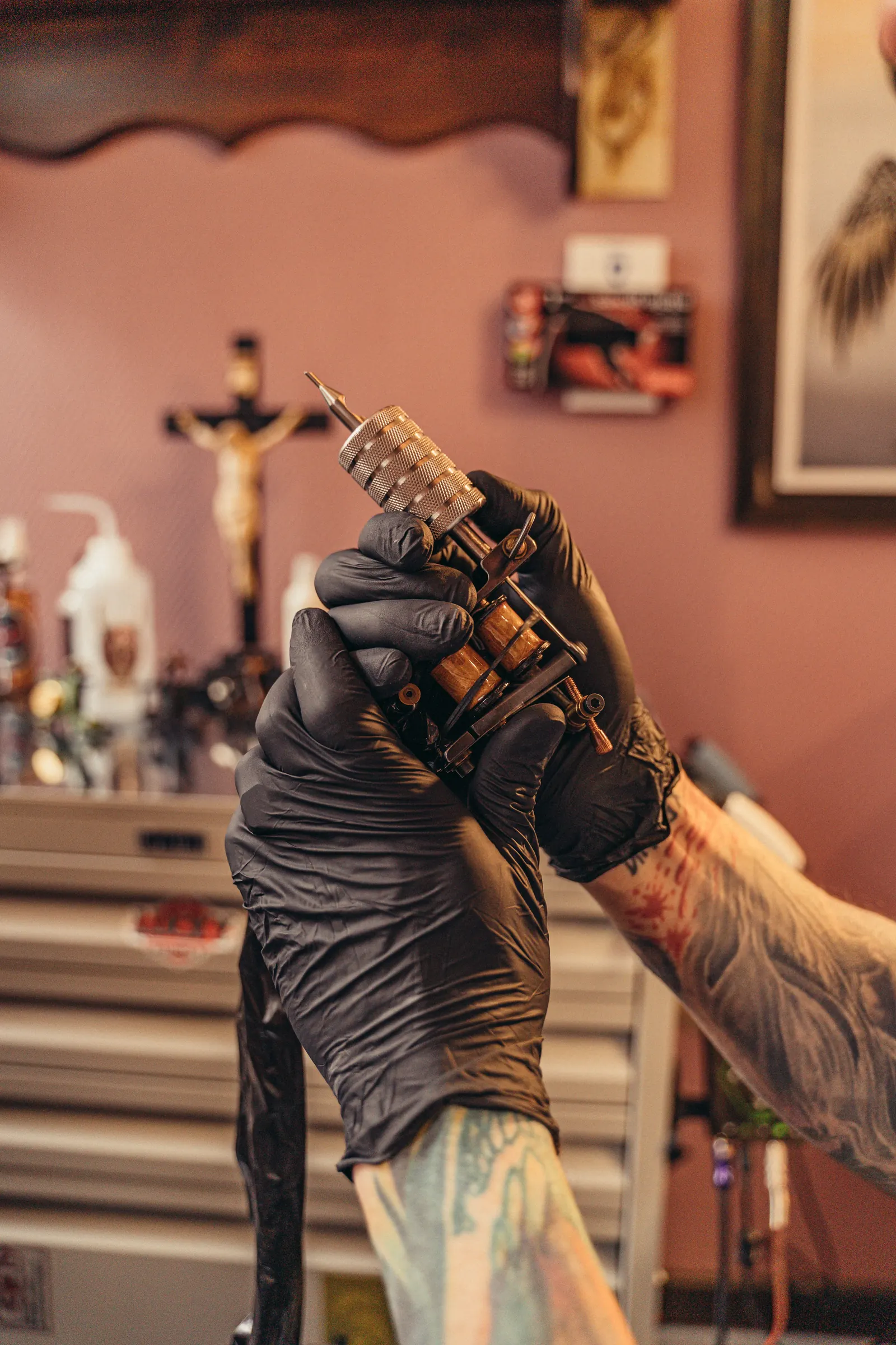 Gloved hands holding a coil tattoo machine in a studio