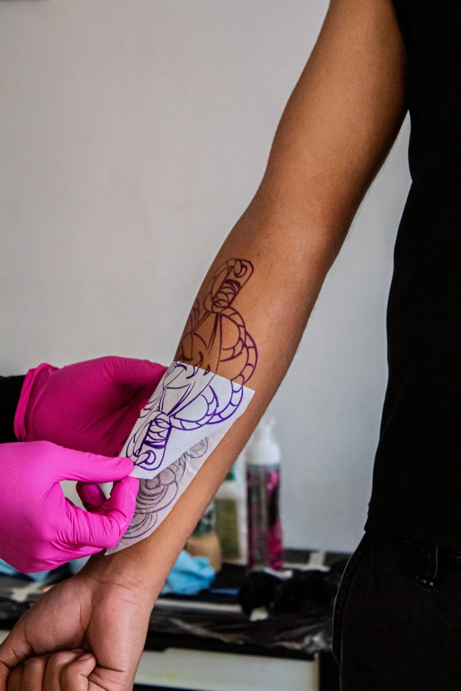 Tattoo artist placing a stencil on a client’s forearm