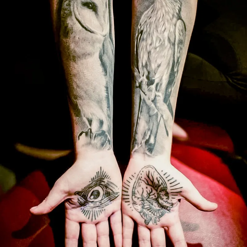 Black and grey owl and hawk tattoos on two forearms, with designs on the palms