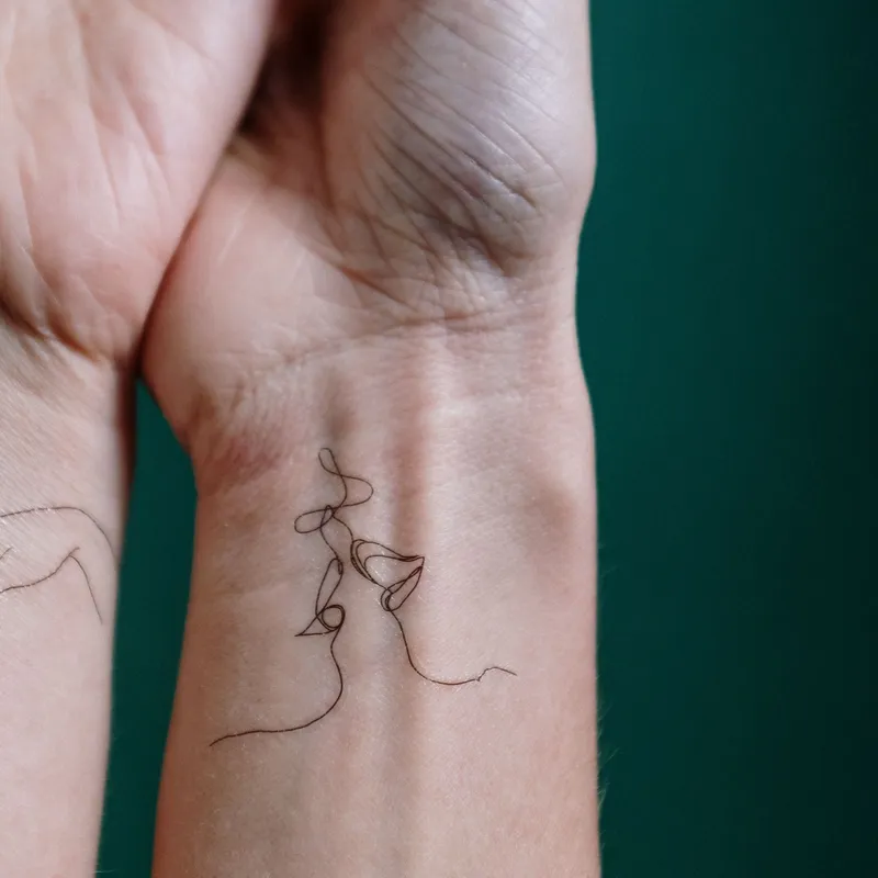 Delicate fine line tattoo of a continuous line drawing on a wrist