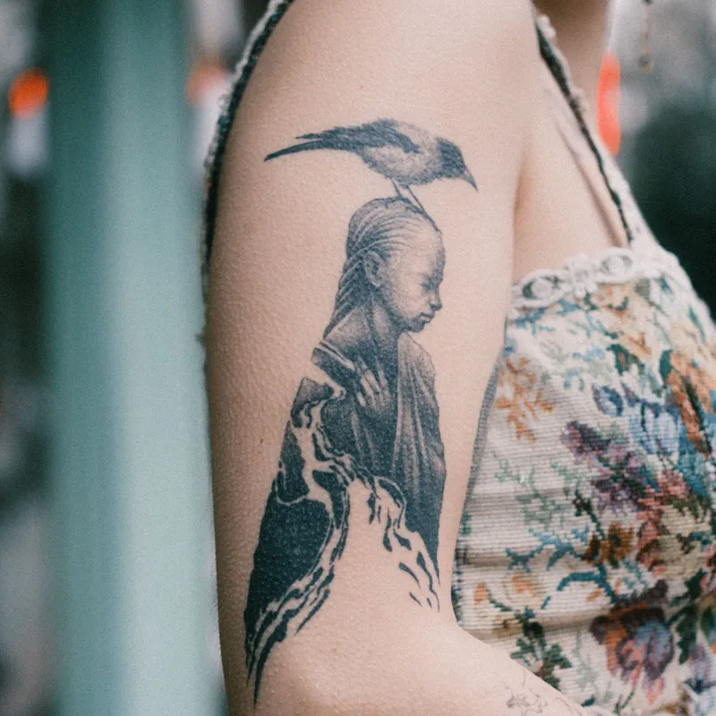 Illustrative black and grey tattoo of a figure with a bird on an upper arm