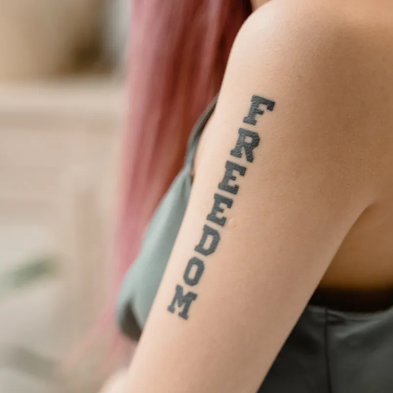 Lettering tattoo of the word Freedom in block letters on an upper arm