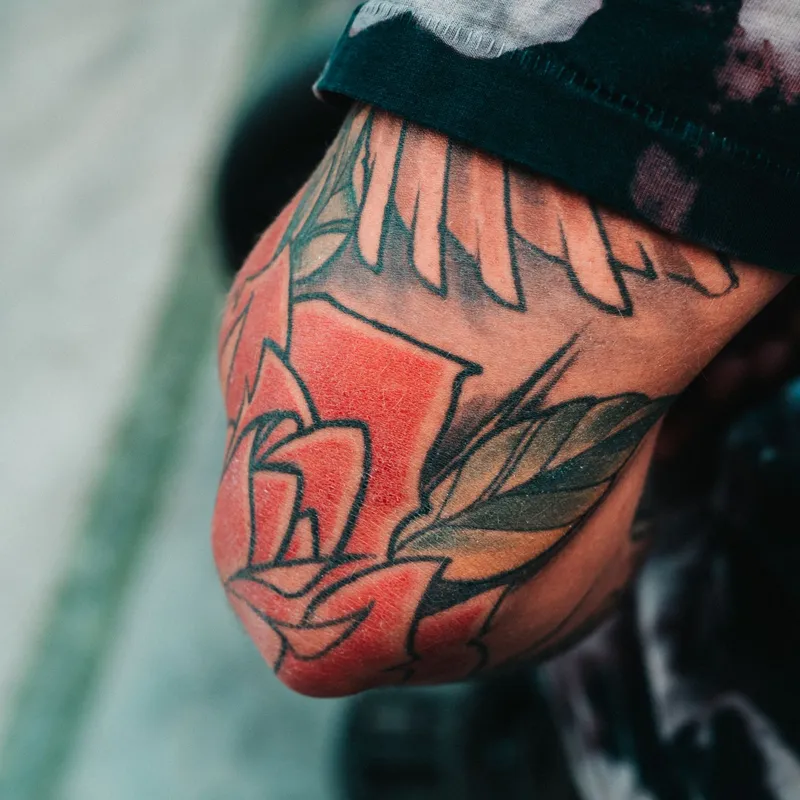 Bold red rose tattoo with leaves and heavy outlines on an elbow
