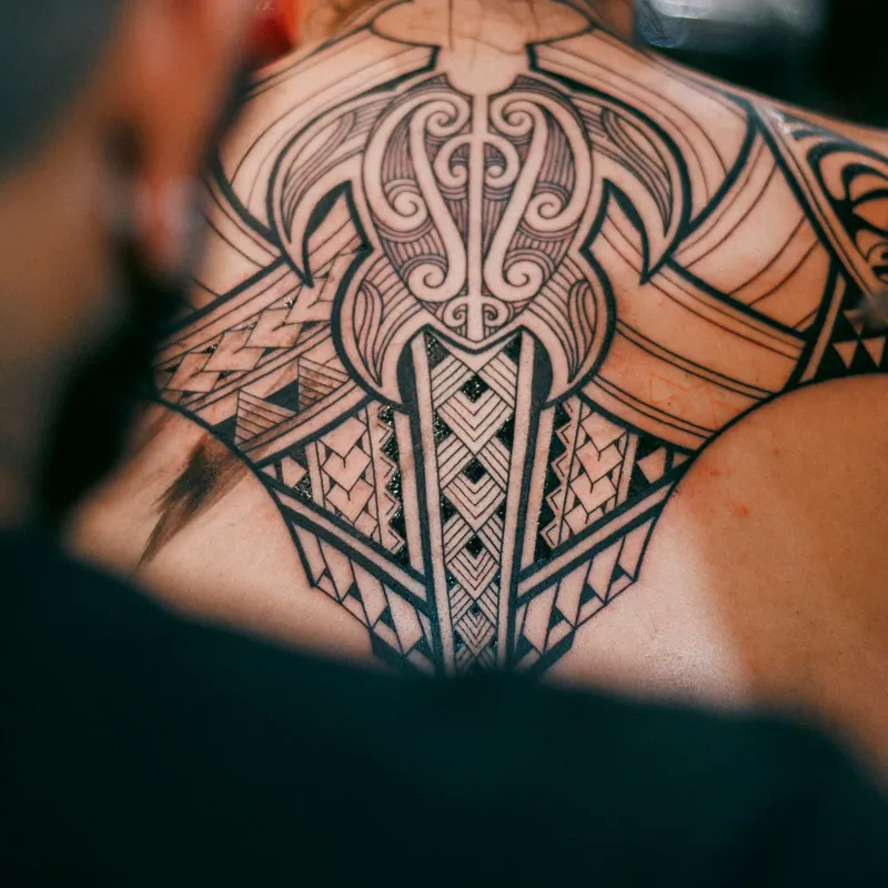 Bold black tribal-style tattoo with Polynesian-inspired patterns across the upper back