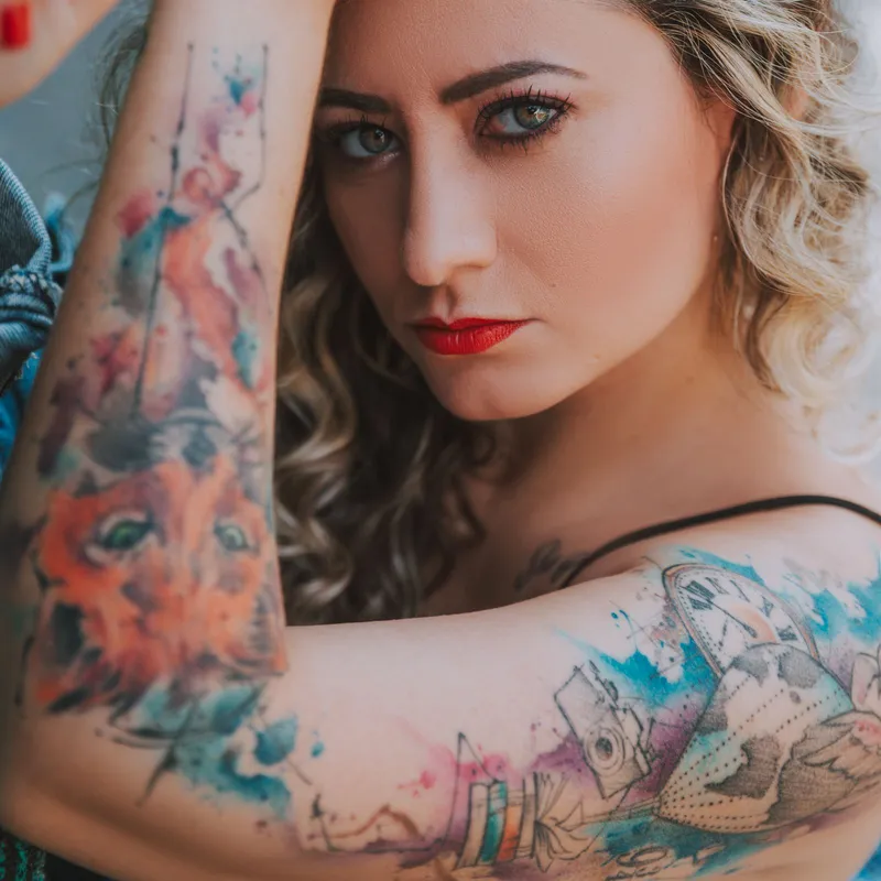 Watercolor-style tattoos with soft splashes of colour on two arms