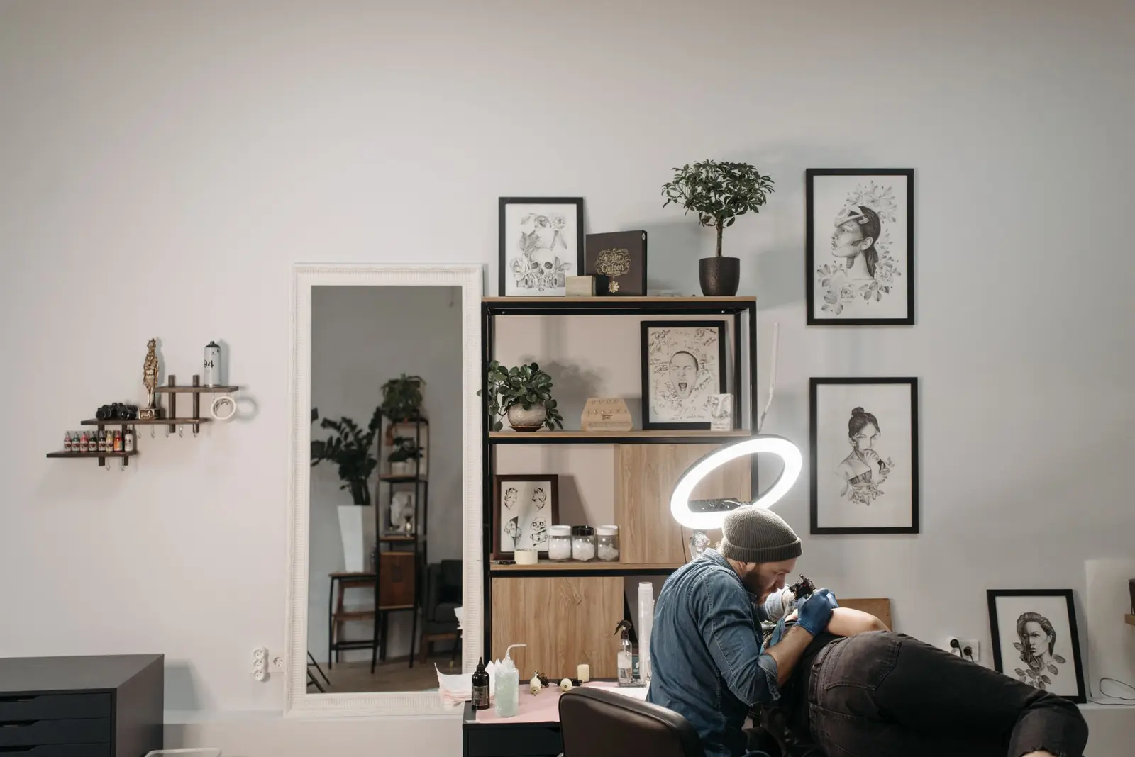 Bright tattoo studio with framed designs on the wall and an artist at work